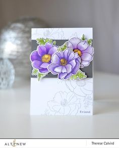 a card with purple flowers on it sitting on a table next to a glass vase