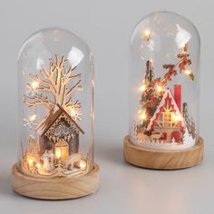 two snow globes with lights on them and a house in the middle one has a christmas scene under it