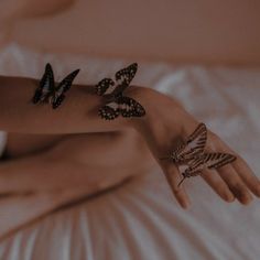 a woman laying on top of a bed covered in tattoos and bracelets with butterflies on her arm