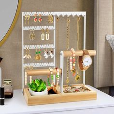 a wooden jewelry rack with earrings and necklaces on it next to a plant in a vase