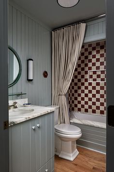 a bathroom with a toilet, sink and bathtub next to a window covered in curtains