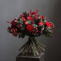 a bouquet of red flowers and pine cones on a wooden stand with berries, greenery and mist