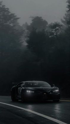 a black sports car driving down a wet road in the dark forest at night time