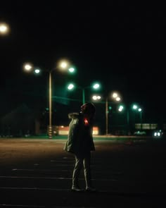 a person standing in the middle of an empty parking lot at night with street lights