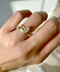 a person's hand holding a ring with a diamond in it and the other hand is wearing a gold band