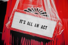 it's all an act sign in front of a red curtain