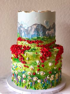 a multi - tiered cake decorated with flowers and mountains