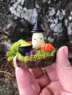 someone holding up a miniature halloween decoration in their hand with moss and pumpkins on it