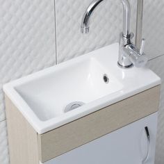 a white sink sitting under a faucet next to a wall mounted toilet paper dispenser