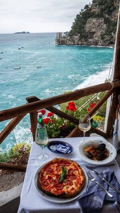 a table with food and drinks on it near the water's edge, overlooking an ocean