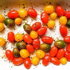 tomatoes and green olives in a pan with seasoning sprinkled on them