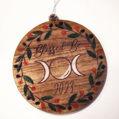 a wooden ornament with two crescents and leaves on the front, hanging from a string