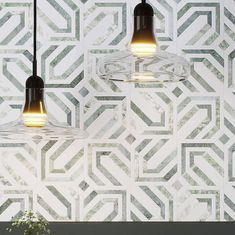 two pendant lights hanging from the ceiling in front of a wall with geometric tiles on it