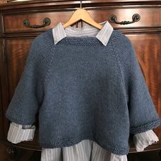 a blue sweater hanging on a wooden dresser next to a white and gray striped shirt