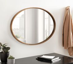 a round mirror hanging on the wall above a desk with a book and potted plant