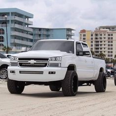 a white truck parked on the beach next to other cars and buildings in the background