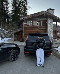 a man sitting on the back of a black van in front of a cabin building