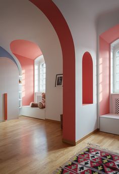 a room with pink and white walls, wooden floors and arched windows in the corner