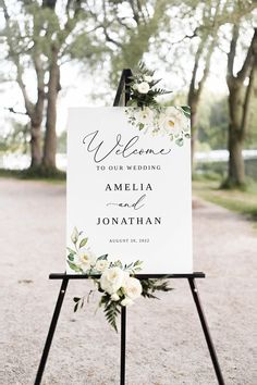 a welcome sign with greenery and white flowers on it in the middle of a gravel road