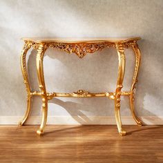 an ornate gold console table against a white wall with wooden floors and wood flooring