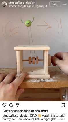 two hands are working on a small wooden toy with wheels and pendulums attached to it