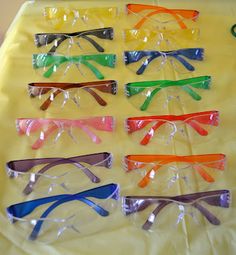 many different colored glasses are sitting on a yellow tablecloth with clear plastic wrap around them