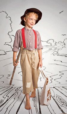 a young boy wearing overalls and a hat with suspenders, holding two bags