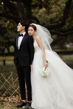 a bride and groom standing in front of a tree