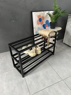 there is a shoe rack on the floor next to a potted plant and an art piece