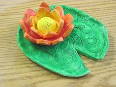 a plastic flower sitting on top of a green leaf covered table next to a wooden surface