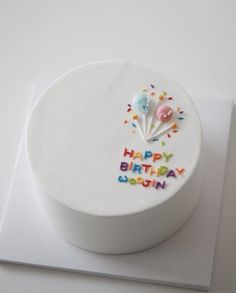 a white birthday cake with colorful sprinkles and balloons