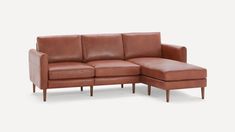 a tan leather sectional sofa with wooden legs and footrests on an isolated white background