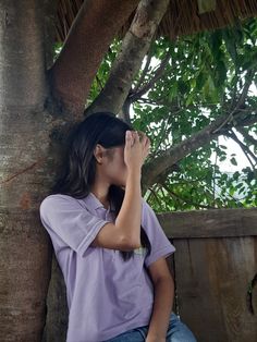 a woman sitting on top of a tree while holding her hand up to her face