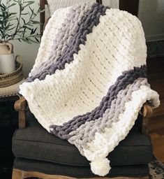 a white and gray blanket sitting on top of a chair next to a potted plant