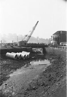 a construction site with pipes laying on the ground next to water and cranes in the background