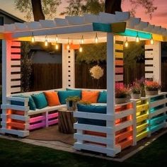 an outdoor seating area made out of pallets and painted in rainbow colors with lights hanging from the roof