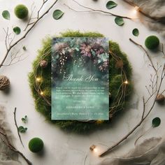 a thank you card on top of a moss covered wreath with lights and greenery