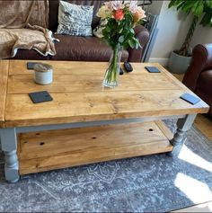 a wooden table sitting in front of a brown couch with flowers on top of it