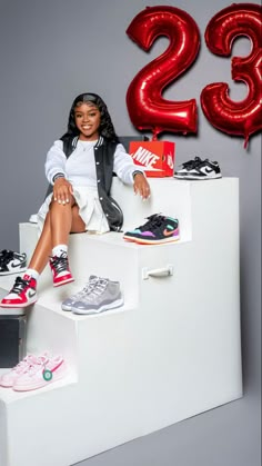 a woman sitting on top of a white step next to red balloons and nike shoes