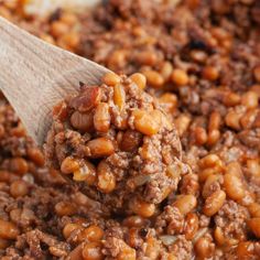 a wooden spoon full of baked beans with meat in the center and ground beef on top