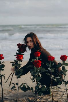 a woman kneeling on the beach with roses in front of her