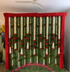 a green wall with red and white flowers hanging from it's sides in front of a ceiling fan