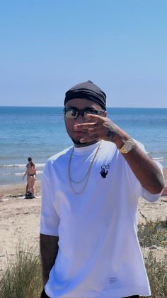 a man standing on top of a beach next to the ocean holding his hand up