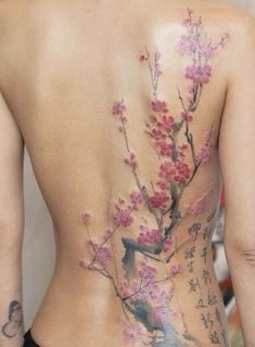 the back of a woman's body with tattoos on it and flowers in bloom