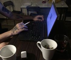 two people sitting at a table with their laptops open and coffee mugs on the table