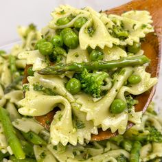 a wooden spoon filled with pasta and peas