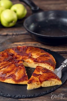 a piece of pizza on a black plate with a spatula and some green apples in the background