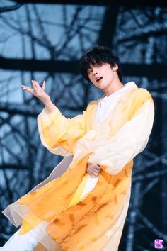 a male in a yellow and white outfit on stage with his hands out to the side