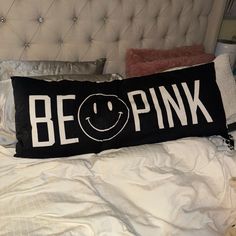 a bed with a pillow that says be pink on it and a smiley face drawn in white