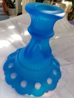 a blue glass vase sitting on top of a white tablecloth covered table with potted plants in the background